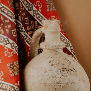 An ancient clay pot displayed beside vibrant traditional patterned fabric, evoking a rustic cultural ambiance.