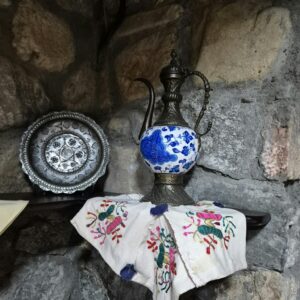Antique metal pitcher with intricate designs on a stone wall shelf.