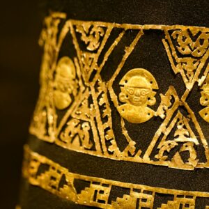 Close-up of a golden Incan artifact with intricate patterns on black background.