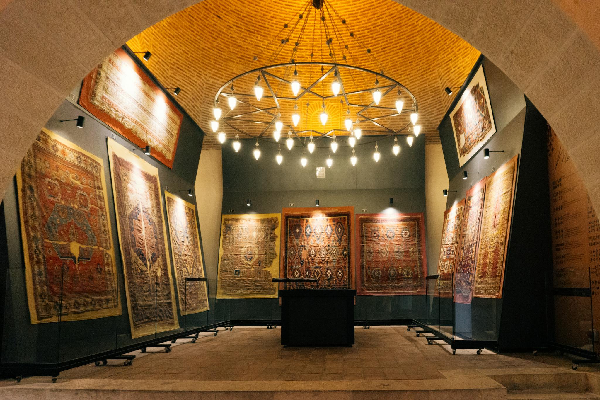Exquisite display of historic rugs in a well-lit interior archway gallery, showcasing intricate patterns and warm ambiance.